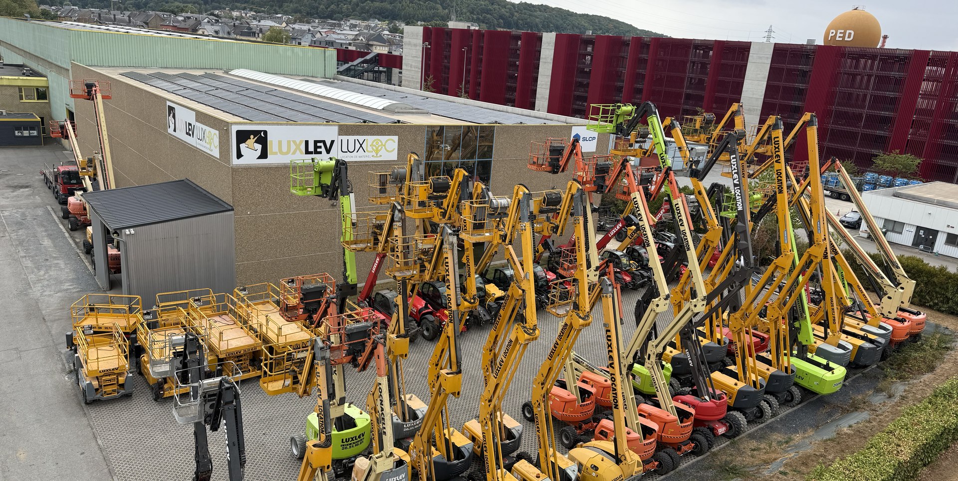 Vue aérienne du dépôt LUXLEV à Pétange : enseigne LUXLEV LUXLOC et parc de nacelles aligné devant le bâtiment